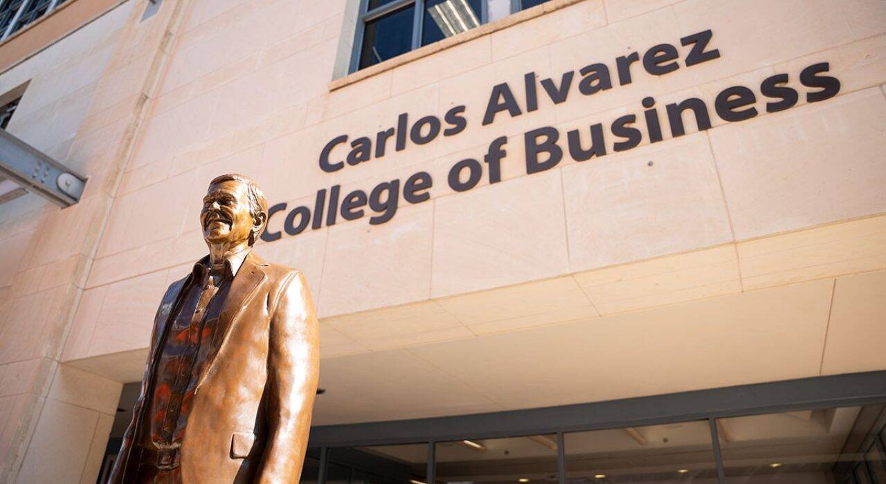 A bronze statue of Carols Alvarez with a sign that reads "Carlos Alvarez College of Business."