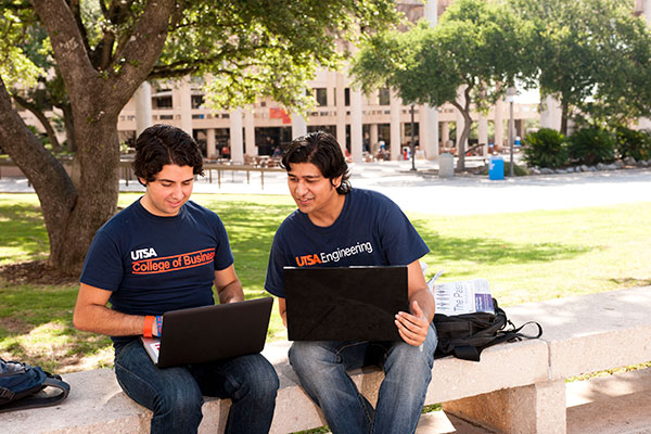 Two students outside on their laptop with blue UTSA shirts