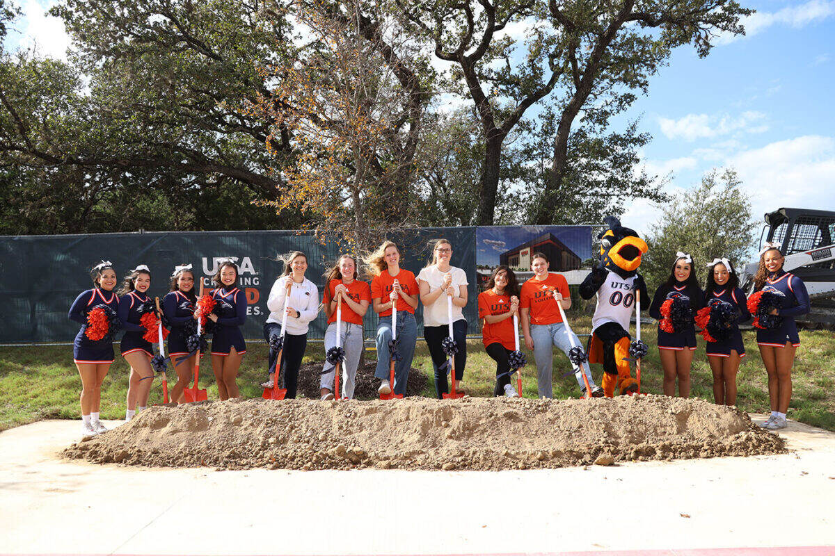 Several people hold shovels in front of a pile of dirt as they pose for a photo.