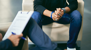 Man sitting down holding his hands across another person.