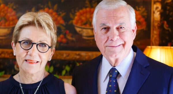 A women in a blue dress and glasses stands beside a man in a blue suit and tie.