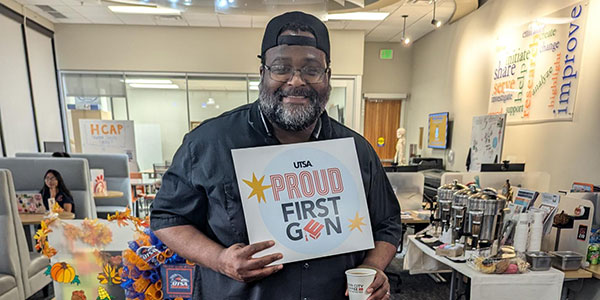 Student with hat backwards holding a Proud First-Gen sign