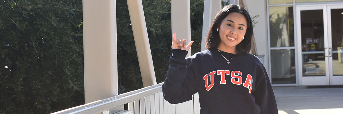 A student in a UTSA sweater doing the roadrunner hand sign