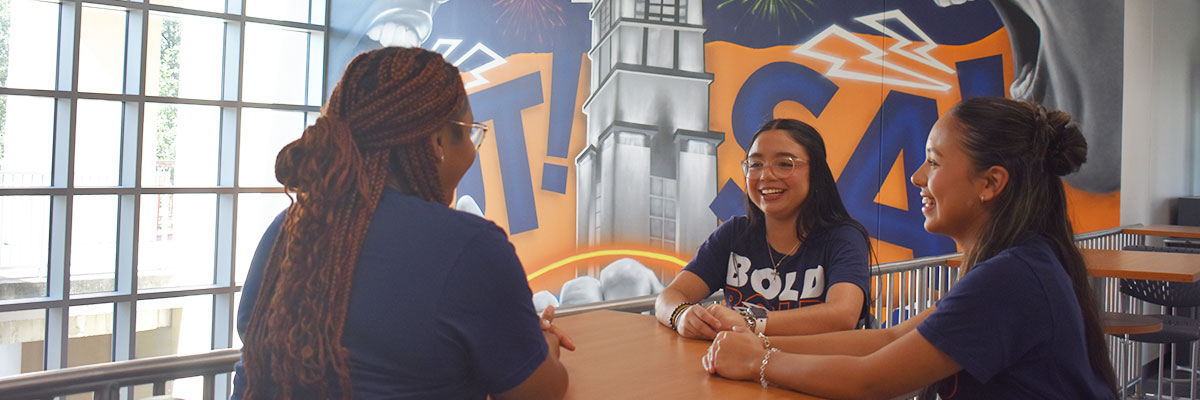 Two students at the Sombrilla with Bold Scholars shirts with both doing the roadrunner hand sign