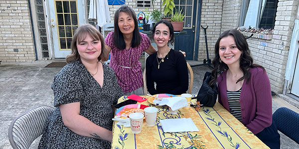Four women smiling outside a home at a table