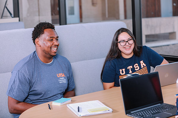 Two students talking to another student with laptops open