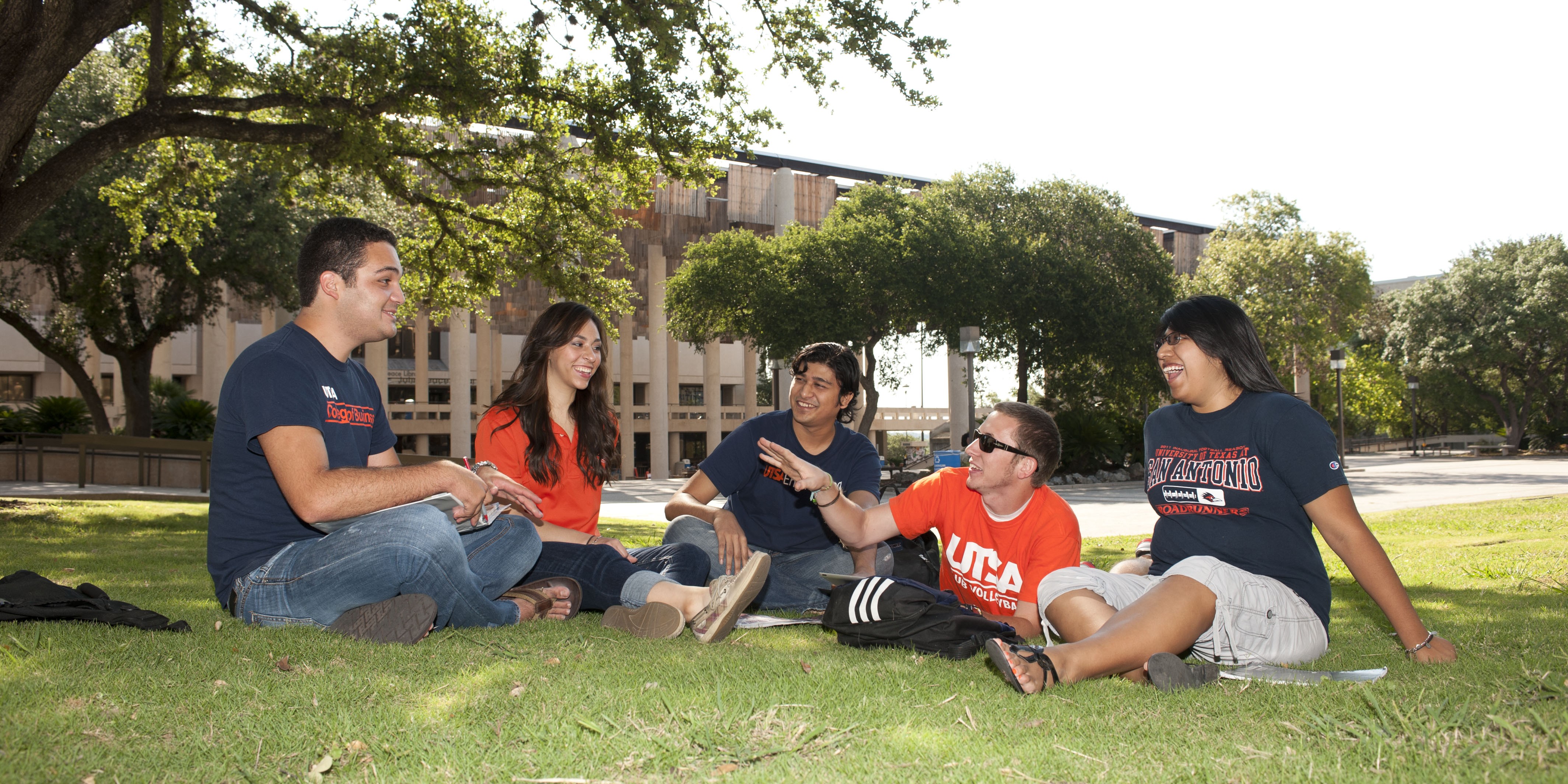 Five students sitting and chatting on the lawn at the main campus
