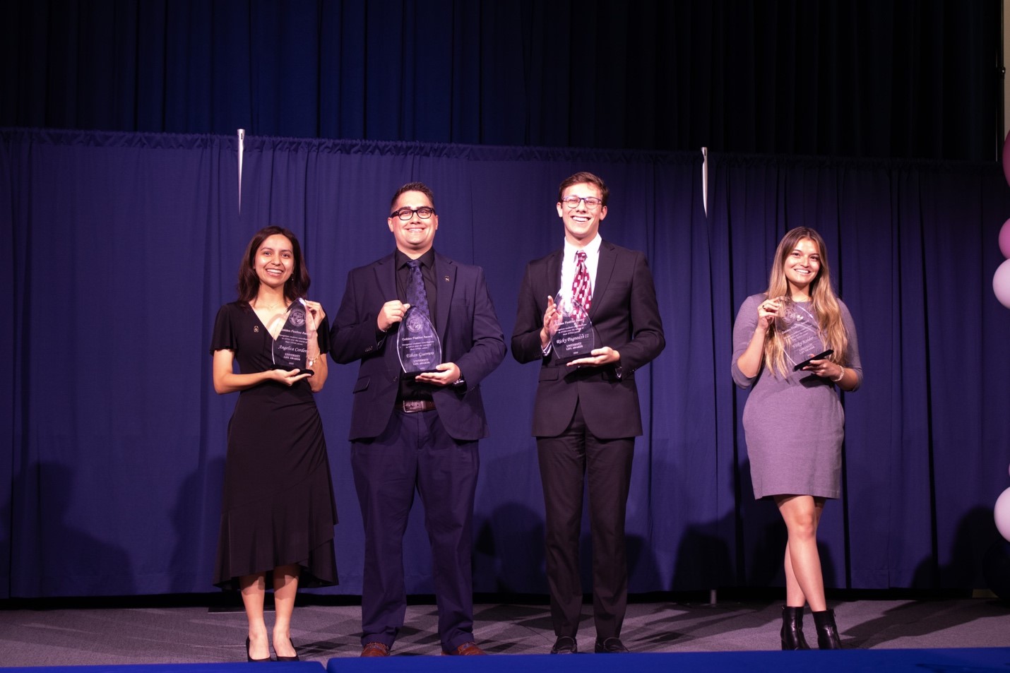 Four students dressed in suits and dresses holding award plaques