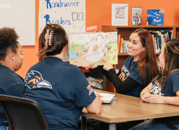 Four people sit around a table in a classroom.