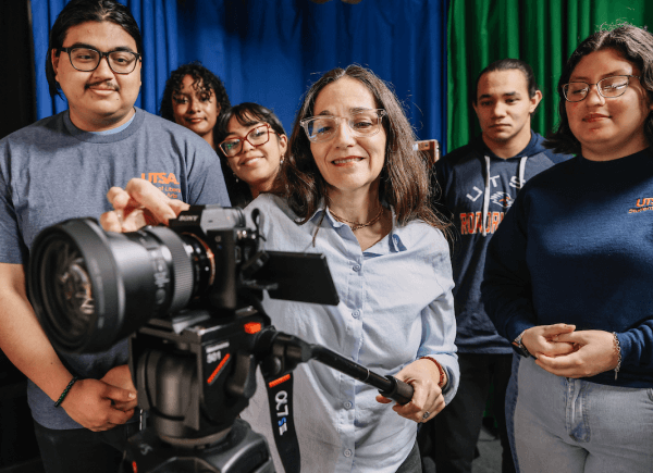 A group of six people, appearing engaged, gather around a camera on a tripod.