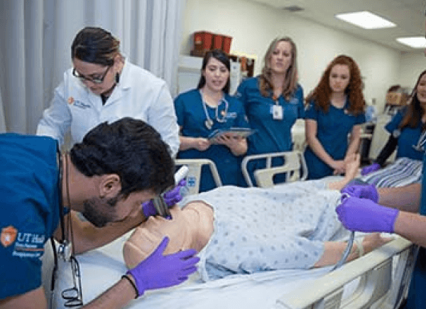Medical students in blue scrubs and a faculty member in a white coat.