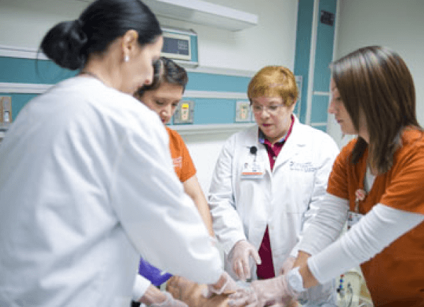 Four medical professionals collaborate around a patient in a hospital room.