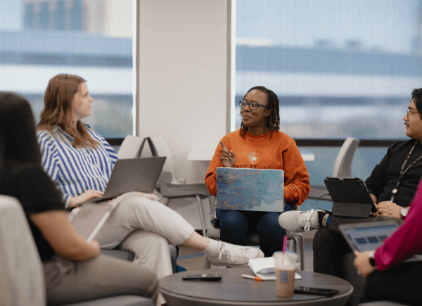 A diverse group of four people sitting in a casual office setting, engaged in discussion.