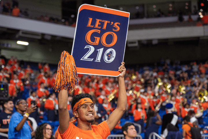 Student holding a 'Let's Go 210' sign at a UTSA Football game