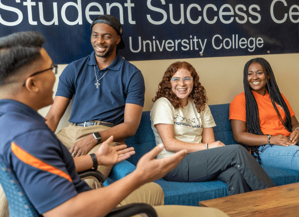 Four diverse students sit on a couch, engaged in a lively discussion.